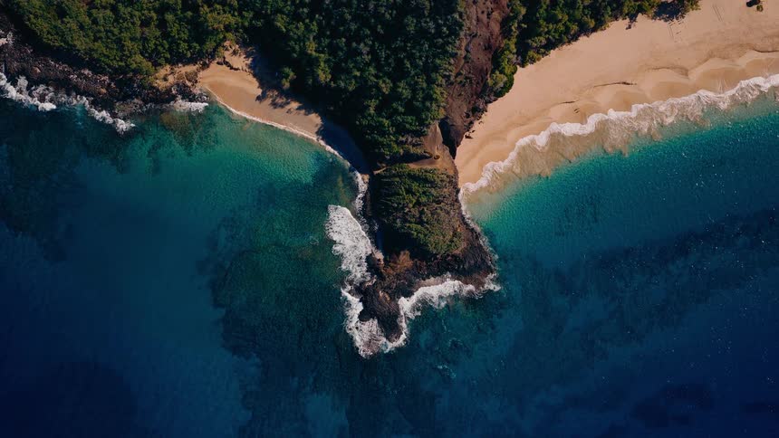 Stunning top-down aerial view of a tropical peninsula with two sandy beaches and vibrant turquoise ocean waters