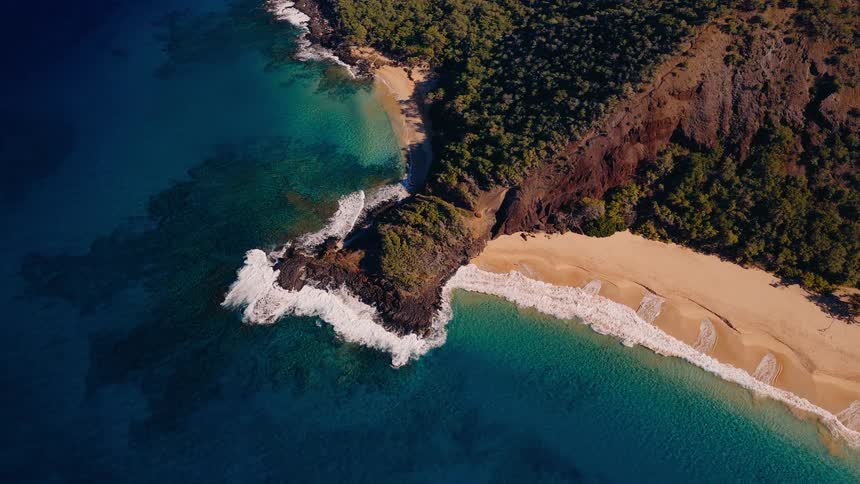 Stunning aerial footage captures a secluded tropical paradise with a lush peninsula separating two pristine golden sand beaches and turquoise ocean waters
