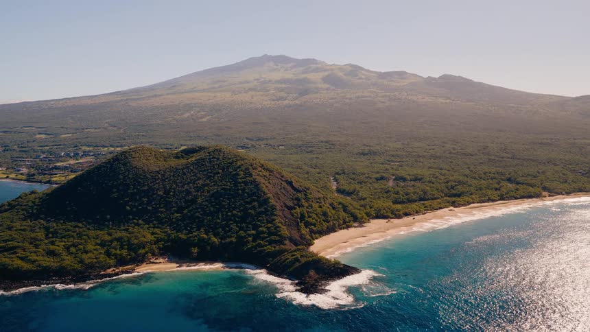 A stunning aerial view of a volcanic island coastline with a cinder cone, sandy beach, and beautiful blue ocean waters