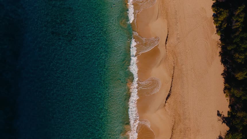 A serene top-down aerial view of turquoise waves gently washing over a beautiful golden sand beach