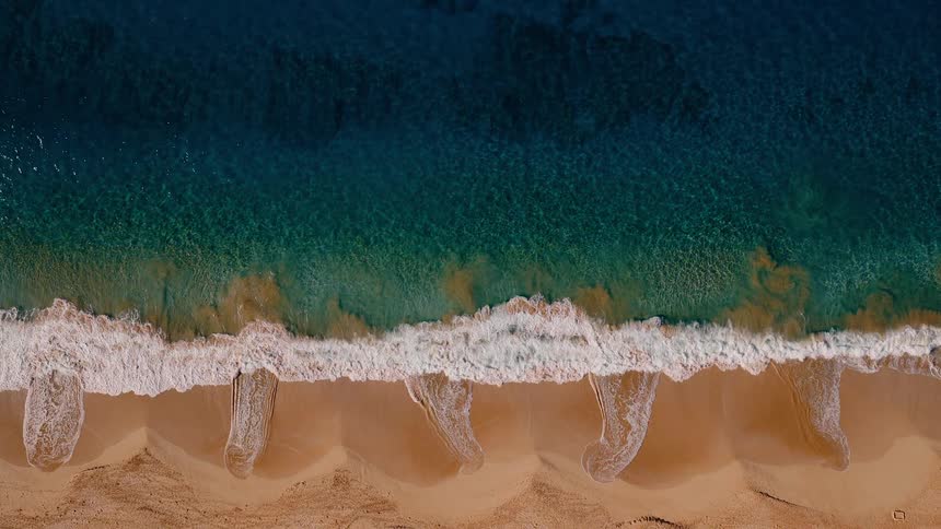 A mesmerizing top-down aerial view of turquoise ocean waves gently crashing onto a golden sandy beach in slow motion