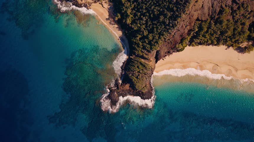 A serene, static aerial view of a tropical island peninsula separating two golden sand beaches with vibrant turquoise and deep blue ocean water