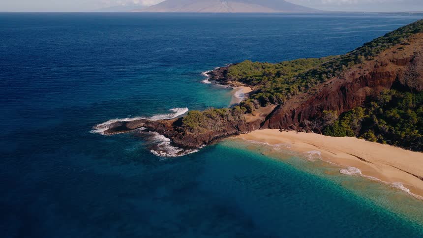 A breathtaking aerial view pulls back from a secluded cove to reveal a stunning tropical island coastline and vast blue ocean