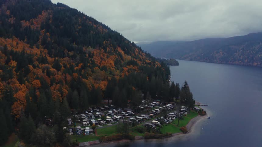 An aerial view pulls back from a lakeside RV park nestled at the base of a mountain covered in colorful autumn foliage