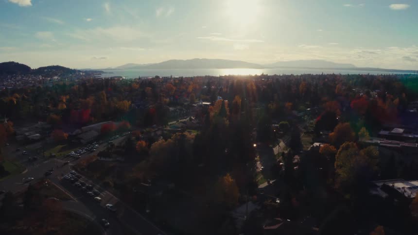 Stunning aerial view of a coastal town during a golden autumn sunset, with colorful trees and traffic flowing on the streets below