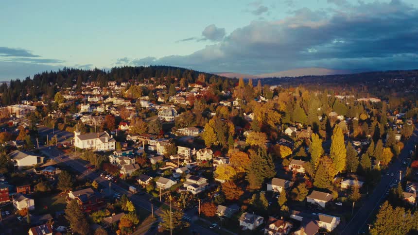 An aerial view pulls back over a charming hillside town basking in the golden light of an autumn evening