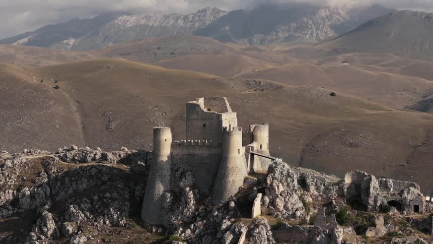 Epic aerial footage slowly pulling back from the medieval Rocca Calascio castle ruins, revealing the vast, mountainous landscape