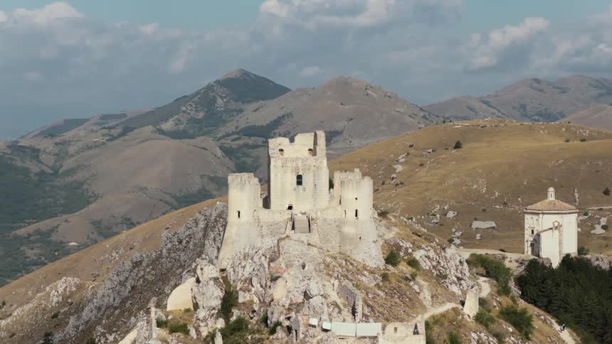 An epic aerial orbit reveals the ancient stone ruins of Rocca Calascio castle perched high in the vast, rolling mountains of Abruzzo, Italy