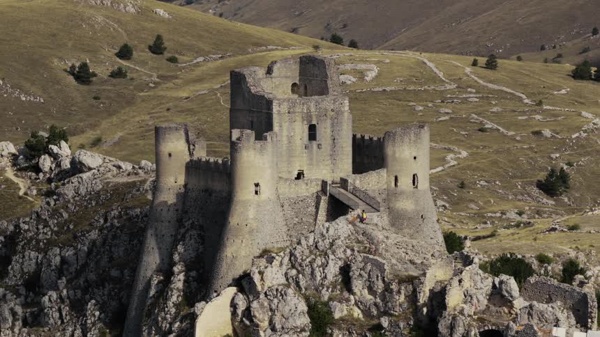 A slow aerial pullback reveals the magnificent ruins of a medieval stone castle perched on a rocky mountain peak