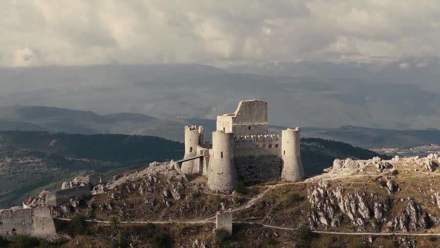 A majestic medieval stone castle in ruins stands atop a rocky mountain as clouds drift by in a time-lapse