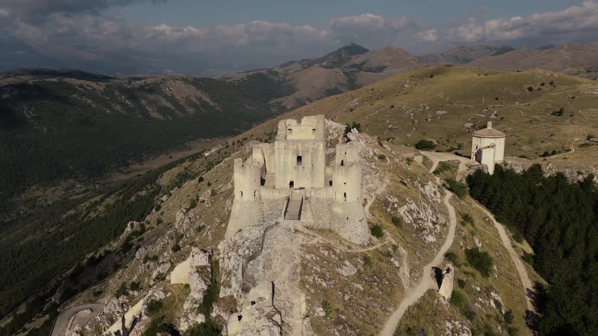 A dramatic aerial shot slowly pulls back to reveal the ancient ruins of Rocca Calascio castle perched on a rugged mountain peak in Abruzzo, Italy