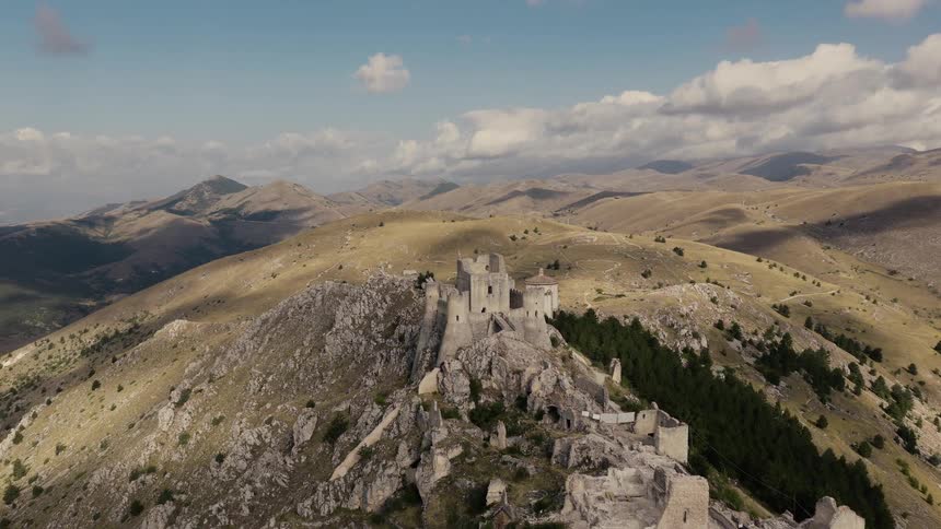 An epic aerial view flying towards the ancient Rocca Calascio castle ruins on a mountaintop in the Italian countryside