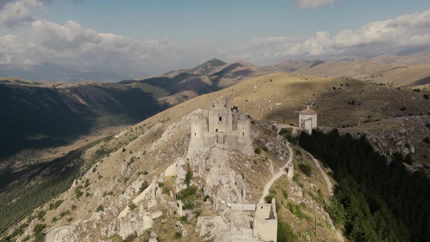 An aerial drone flies towards the ancient ruins of Rocca Calascio castle on a mountaintop in the Abruzzo region of Italy