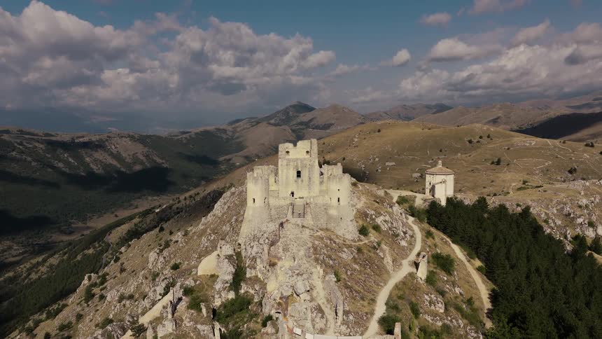 A stunning aerial shot pulls back from the ancient ruins of Rocca Calascio Castle, revealing the vast mountain landscape of Abruzzo, Italy