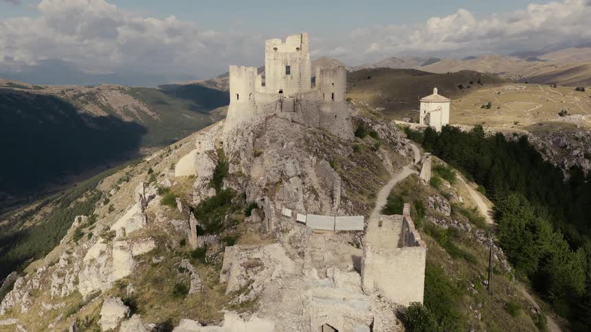 An epic aerial shot pushes in on the ancient stone ruins of Rocca Calascio castle perched atop a mountain in Abruzzo, Italy