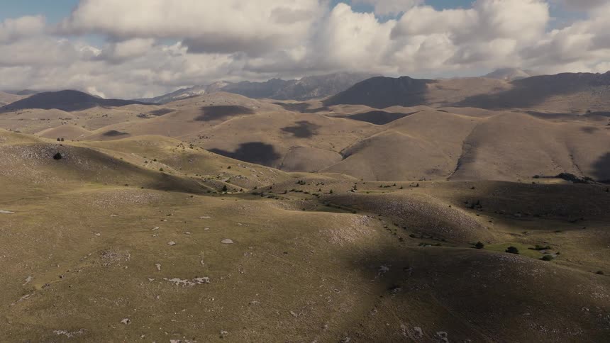 A serene aerial view of a rugged mountain landscape with rolling hills and cloud shadows