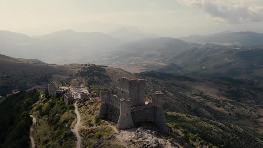 An epic aerial flight over the ancient ruins of a medieval castle perched atop a rugged mountain