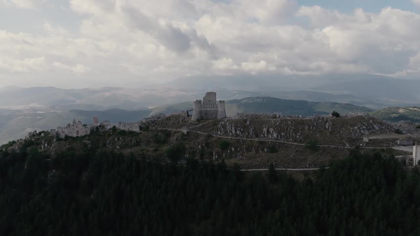 A majestic aerial flight approaches and soars over the ancient Rocca Calascio castle ruins nestled in the Italian mountains