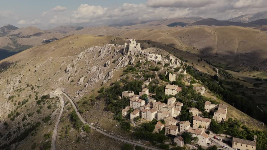 Aerial drone footage flies towards the ancient, ruined castle of Rocca Calascio and its village, perched on a mountaintop in the Italian Apennines