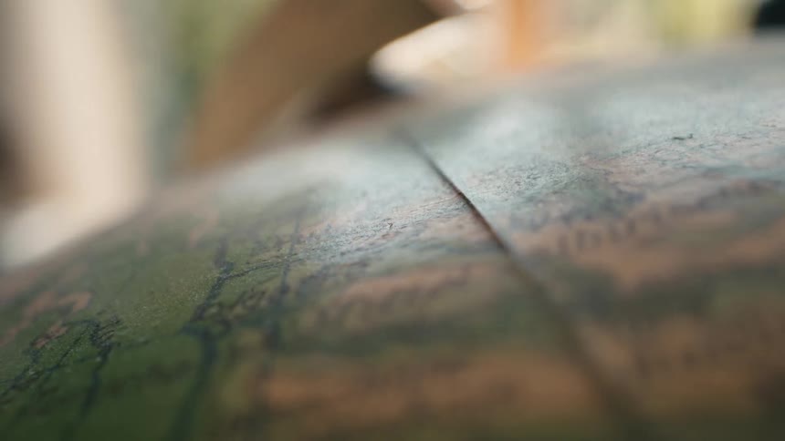 A close-up rack focus shot reveals the map details on an antique, dusty globe