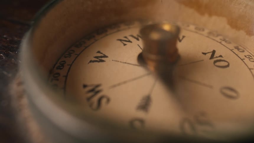 A macro shot shows the needle of an antique compass spinning wildly, failing to find its direction