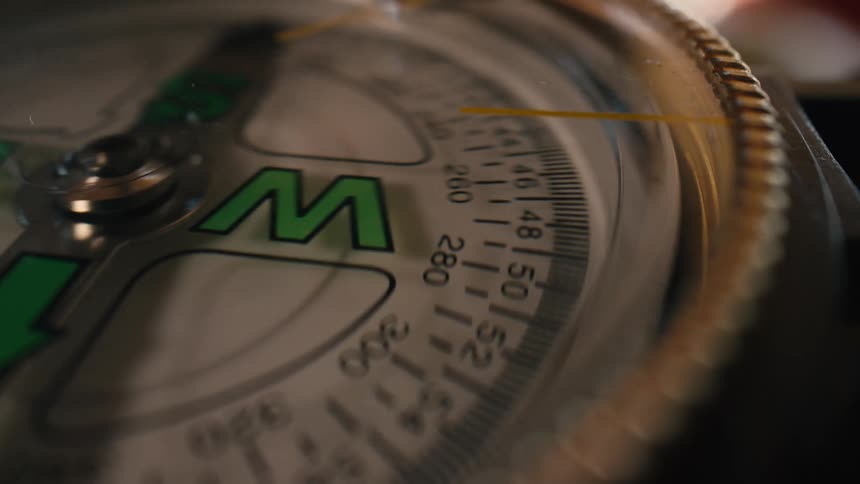 Macro shot of a spinning compass dial, erratically moving past West