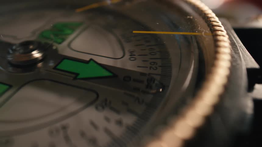 The needle of a magnetic compass spins around the dial in a dramatic close-up shot