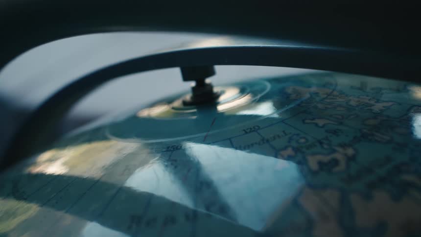 A moody close-up shot shows the top of a globe spinning on its axis with a glossy reflection
