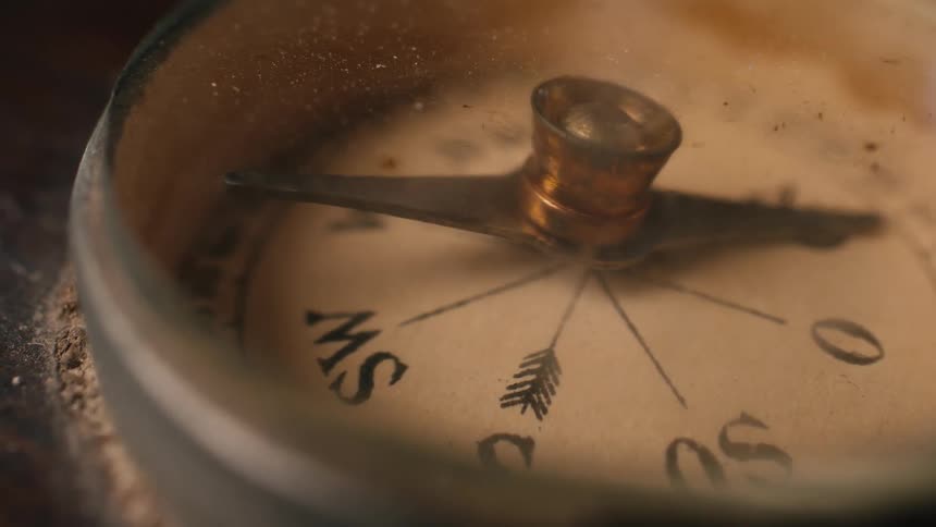 A close-up macro shot of a dusty, old, vintage compass with the arrow spinning erratically, searching for direction