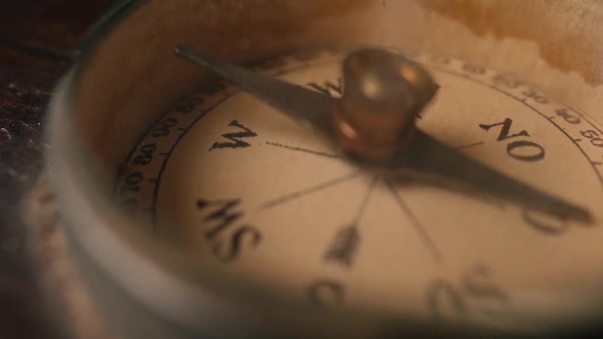 A close-up of an antique compass with its needle spinning wildly and searching for direction