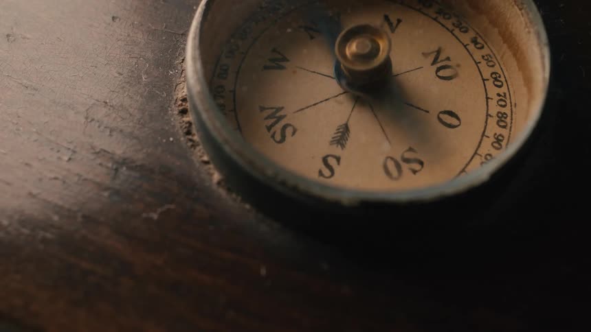 Close-up of an old, dusty compass with a frantically spinning needle set into a dark wooden surface