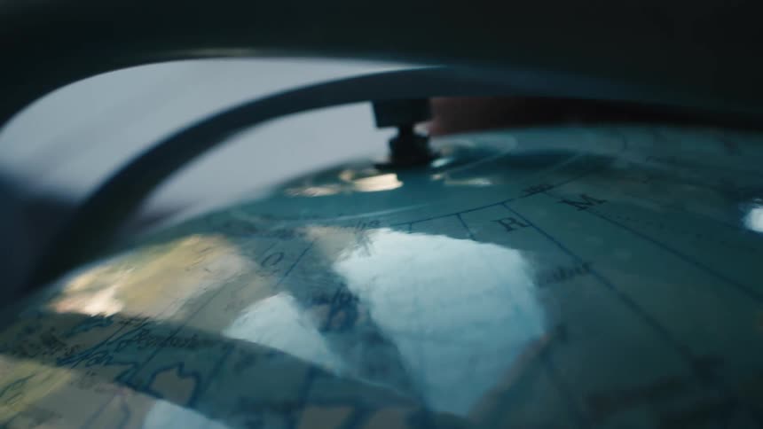 A close-up of a vintage globe spinning on its axis in a moody, low-light setting