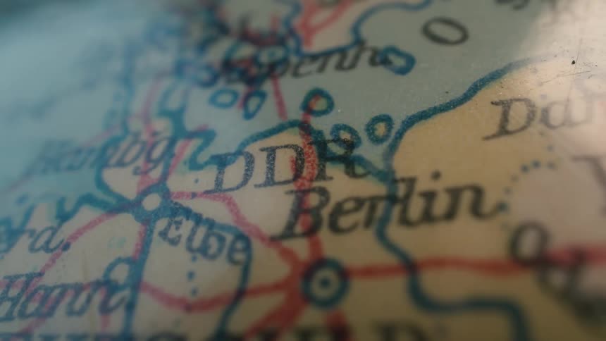 A close-up shot of a vintage world map focuses on the German Democratic Republic (DDR) and its capital, Berlin