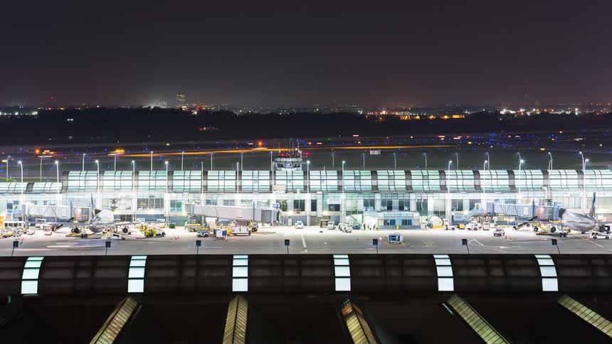 Nighttime timelapse of a bustling airport terminal with planes taking off and landing as ground crew works on the tarmac