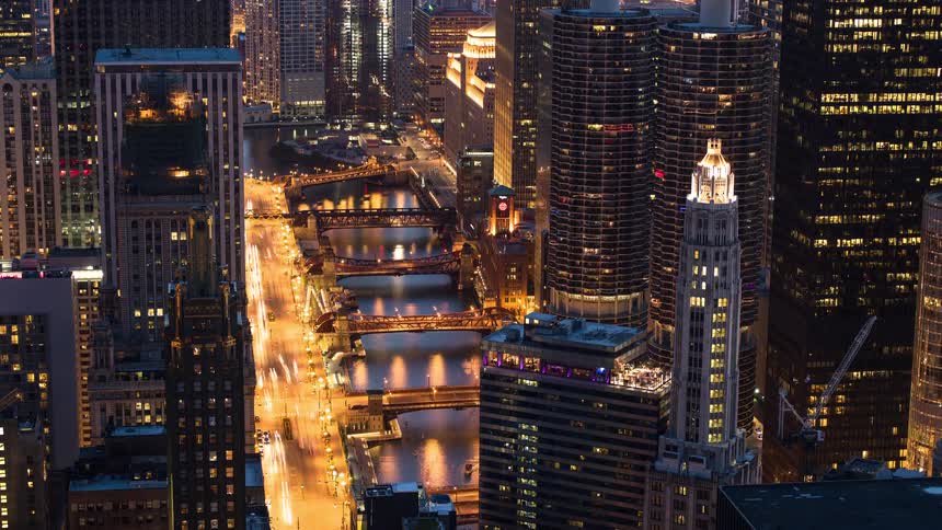 An elevated time-lapse of the bustling Chicago River as the sun sets and the city lights begin to illuminate the downtown skyline