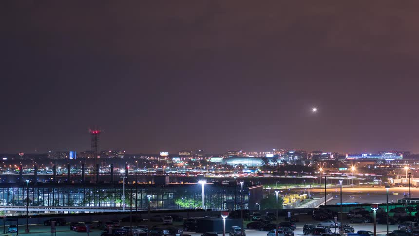 Dynamic night timelapse of a busy airport with airplanes taking off and landing over a bustling city skyline