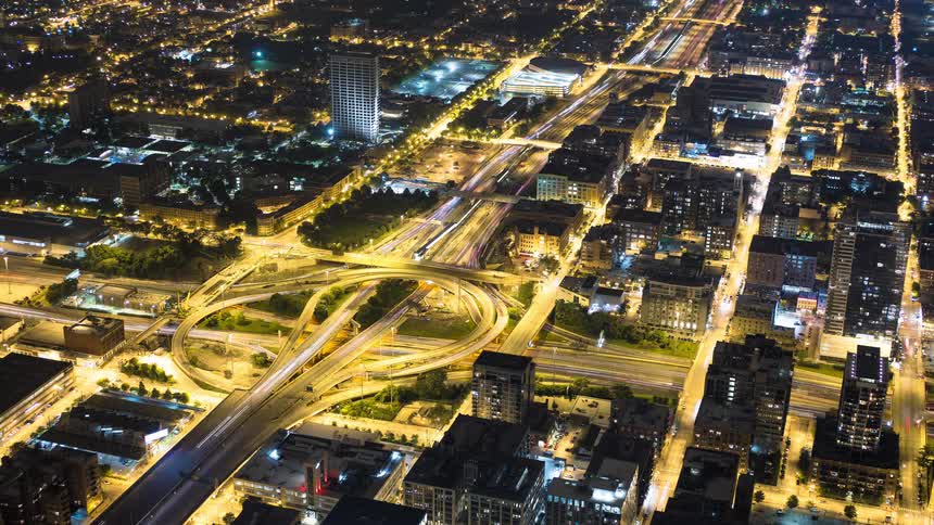 A stunning high-angle time-lapse of a major city's bustling highway interchange at night, with traffic creating beautiful light trails