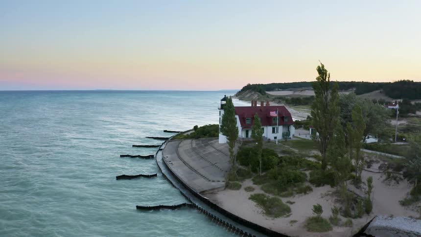 Aerial pull-back shot of the scenic Point Betsie Lighthouse on the sandy coast of Lake Michigan at sunset