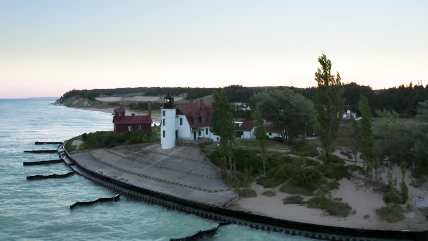 An aerial view pulls away from the historic Point Betsie Lighthouse as its beacon shines over the windy shores of Lake Michigan at dusk
