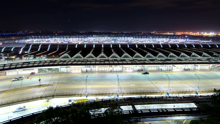 Night time-lapse of a busy international airport terminal with traffic streaming by on the highways below