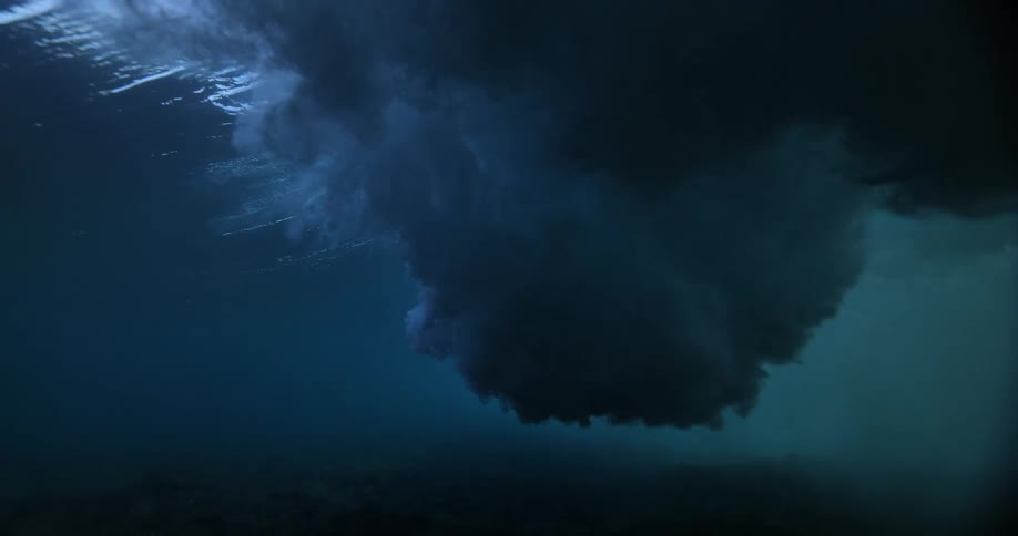 A powerful ocean wave breaks in dramatic slow motion as viewed from underwater, creating turbulent clouds of bubbles