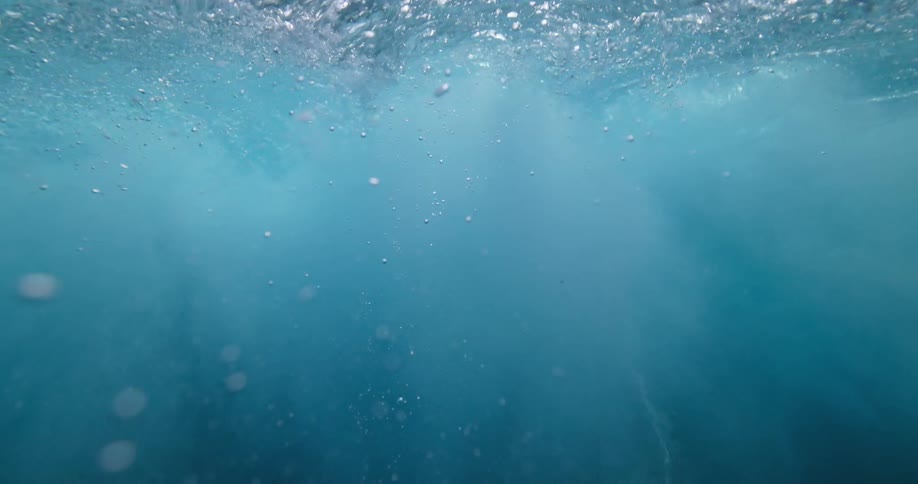A slow-motion underwater perspective of turbulent blue water and rising air bubbles