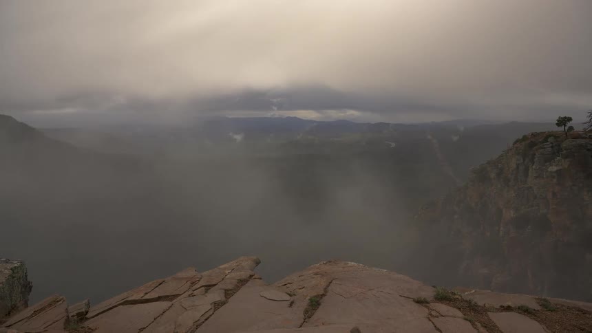 A dramatic pan across a misty canyon as storm clouds and fog slowly clear to reveal the vast landscape below