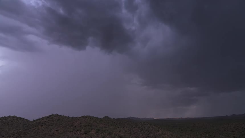 A wide shot of a massive dark storm cell over a desert mountain range with constant in-cloud lightning strikes