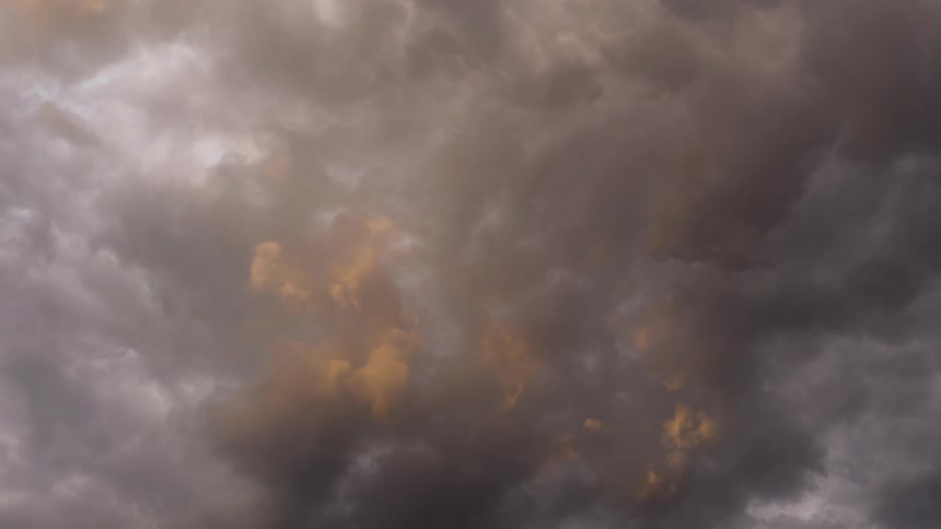 Dramatic, dark storm clouds swirl slowly across the sky, backlit by a faint golden glow