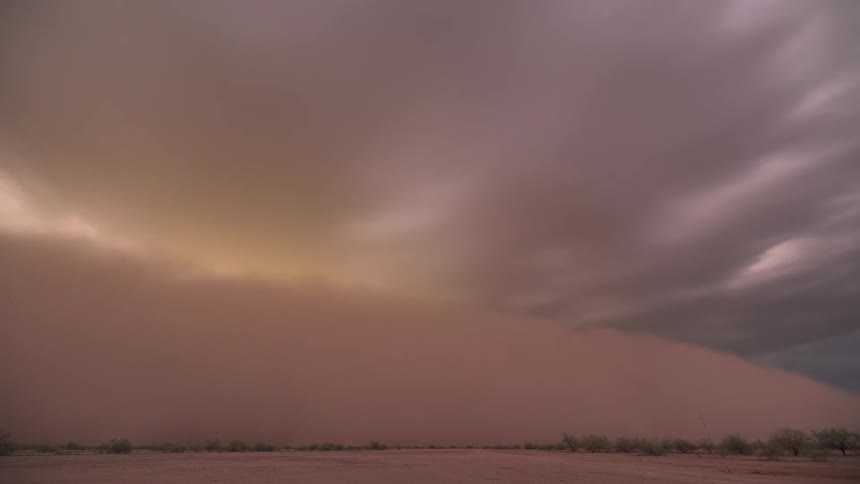 A massive sandstorm, known as a haboob, rolls across the desert landscape, completely engulfing the view in a thick wall of dust