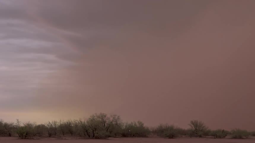 A massive haboob, or dust storm, with lightning flashing within its clouds, engulfs a desert landscape at dusk