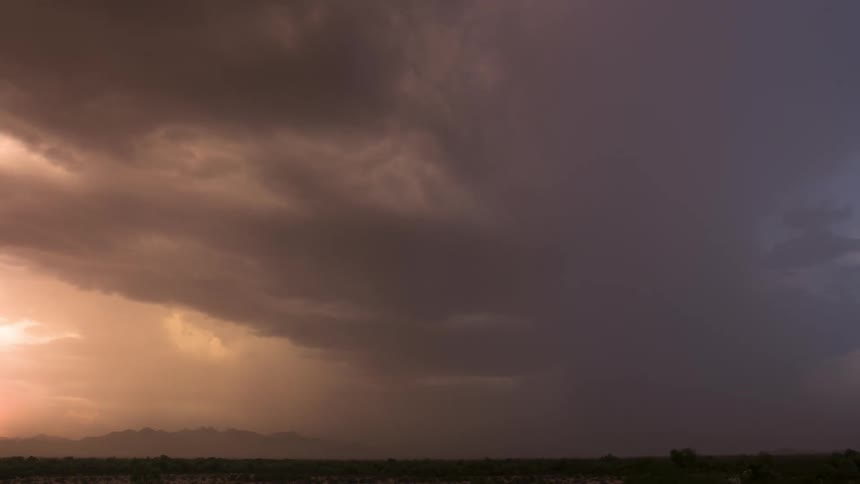 Ominous storm clouds gather and flash with lightning over a mountain range during a vibrant sunset