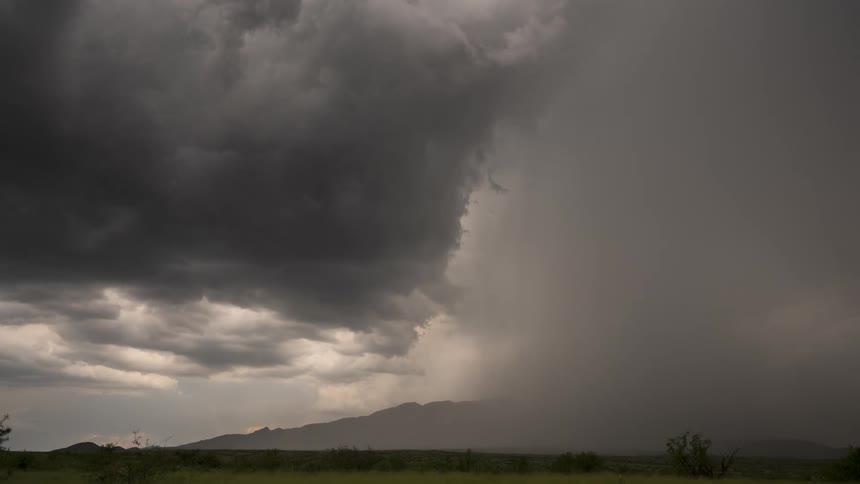 A powerful and ominous thunderstorm unleashes a wall of rain over distant mountains