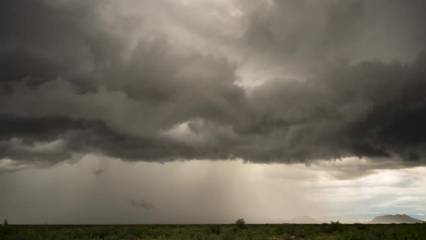 Time-lapse of ominous dark storm clouds gathering and releasing a downpour over a vast, green landscape